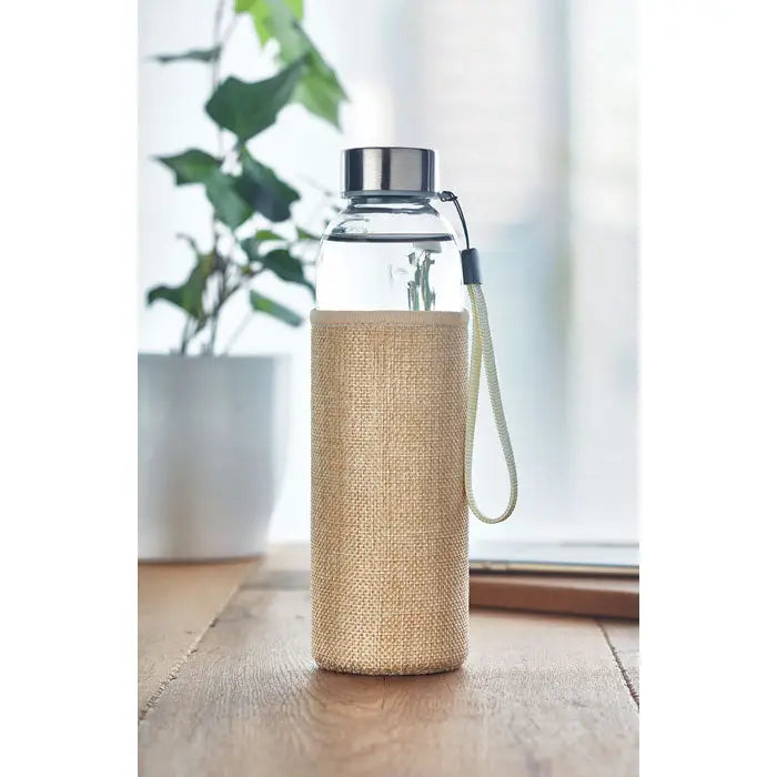 Sticlă de sticlă de 500 ml cu capac metalic argintiu și curea verde deschis în husă de in bej texturat