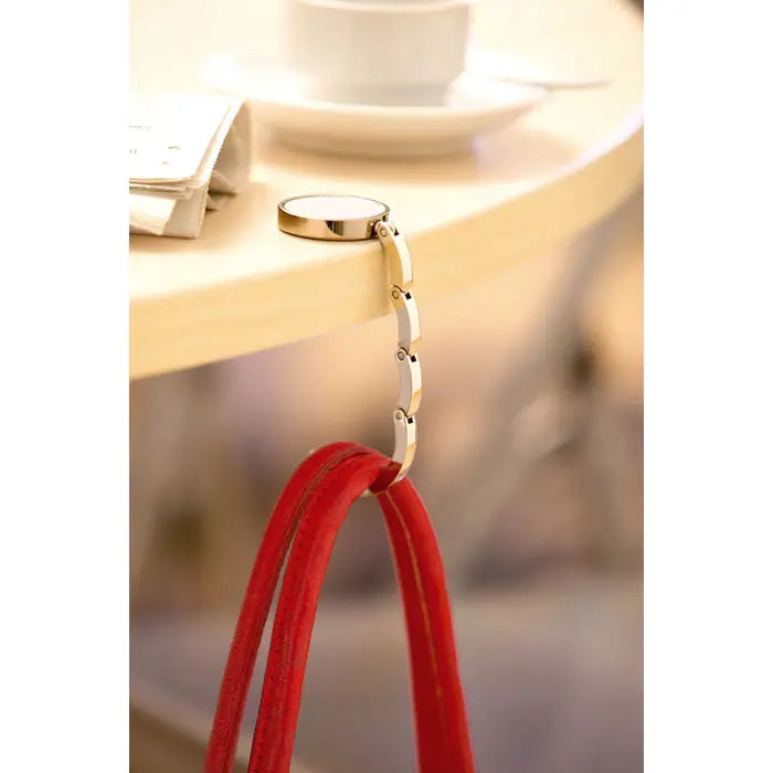 Suport geanta de mana pentru biroul tau metal auriu cu design circular si lant segmentat tine barete rosii din piele intoarsa