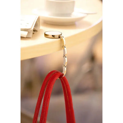 Suport geanta de mana pentru biroul tau metal auriu cu design circular si lant segmentat tine barete rosii din piele intoarsa