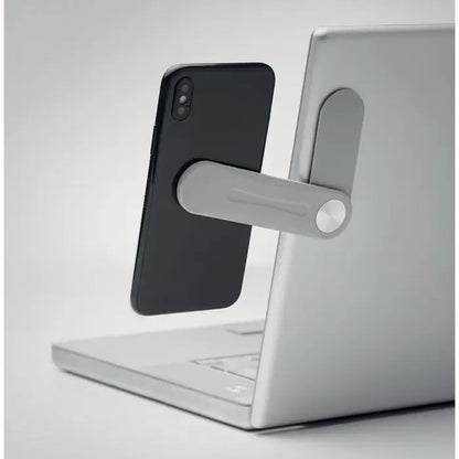 Suport magnetic gri pentru telefon din metal ținând un smartphone negru vertical lângă un laptop argintiu