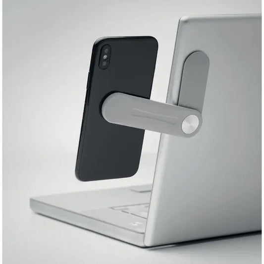 Suport magnetic gri pentru telefon din metal ținând un smartphone negru vertical lângă un laptop argintiu