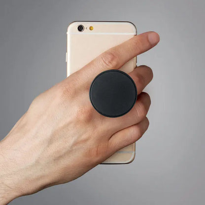 Suport rotund negru din plastic pentru telefon atasat pe spatele unui smartphone auriu tinut in mana