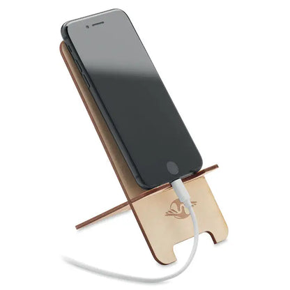 Suport telefon din lemn de mesteacan deschis cu logo pasare gravat laser, sustinand un telefon negru cu cablu alb de incarcare